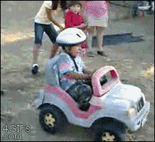 A little girl pushes her unwilling brother down a hill in his power wheels