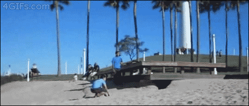 Two guys are doing flips at a beach and one of them lands on top of the other