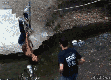 A guy jumps onto a girl hanging upside down on a rope causing them both to fall