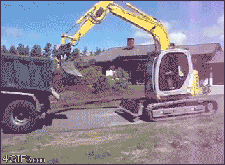 An excavator loads into the back of a truck by pushing itself up with the bucket