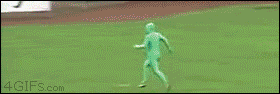 A man dressed in an all green suit is chased around the field during a baseball game