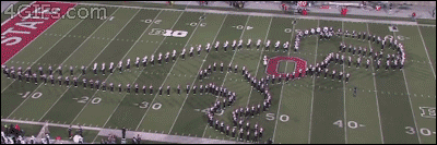 A marching band forms a walking tyrannosaurus rex from an aerial view
