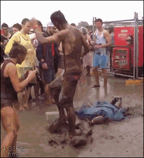 A guy does the worm dance in the mud and rain at a concert