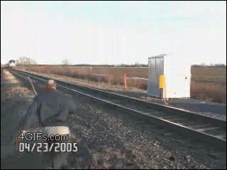 A guy slips on train tracks while a train is coming at him
