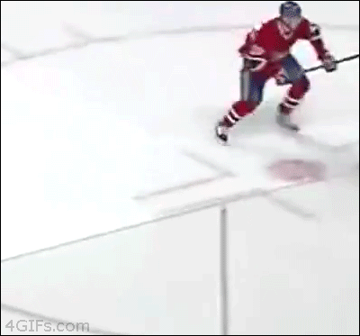 A kid at a hockey game falls down when players hit the plexiglass he's pressed against