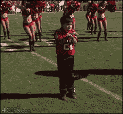 A kid dances with cheerleaders at a football game