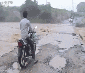 A guy tries to ride a motorcycle across a flooded area and is swept away