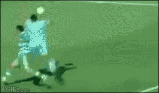 A soccer player scores a goal while lying on his back after falling