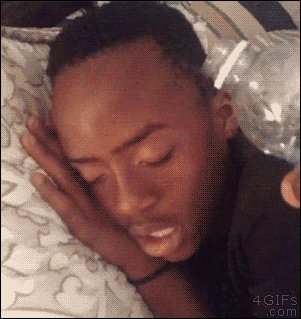 A guy's friend pours water on his face while he's sleeping