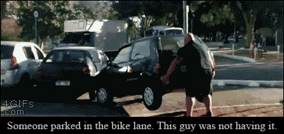 A strong bicyclist moves a car parked in the bike lane