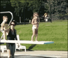 A boy pushes a hesistant girl on the diving board into the pool