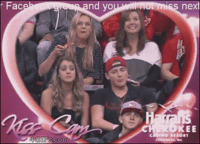 A girl devours pizza in the background of a Kiss Cam