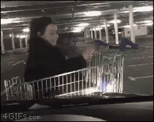A girl in a shopping cart gets pushed by a car for fun
