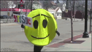 A person in a smiley face costume falls and can't easily get up